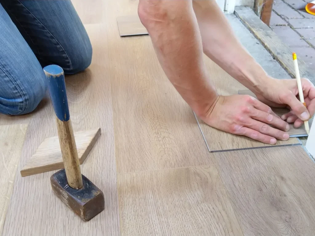 Iemand legt een laminaatvloer en tekent een plank af met een potlood