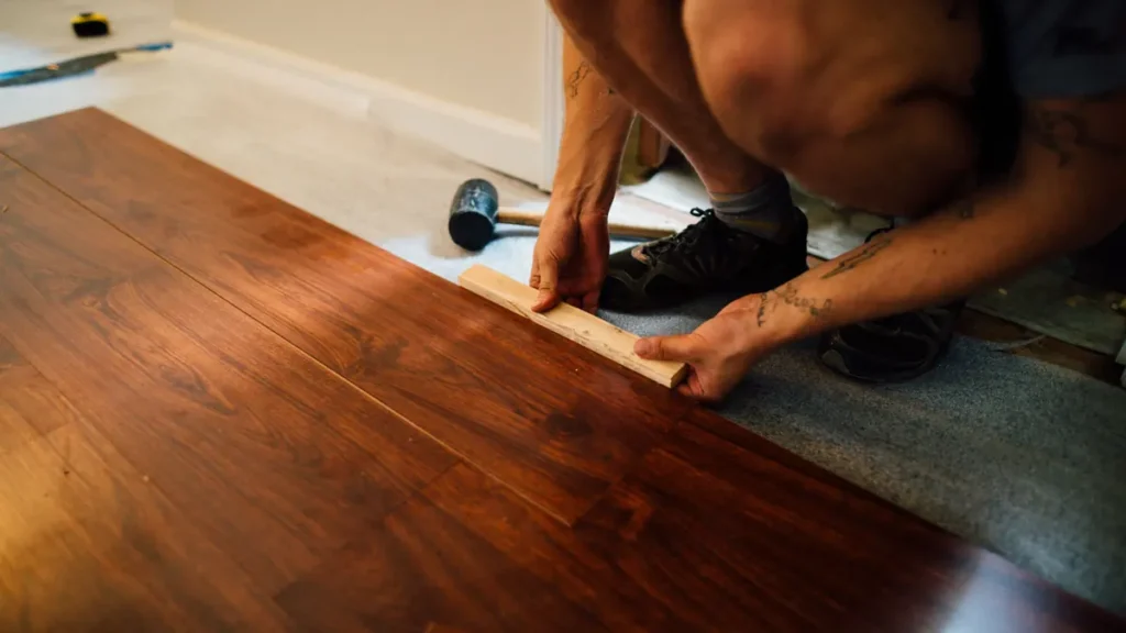 Iemand drukt donkere laminaatplanken aan met een houten klosje, met een rubberen hamer ernaast