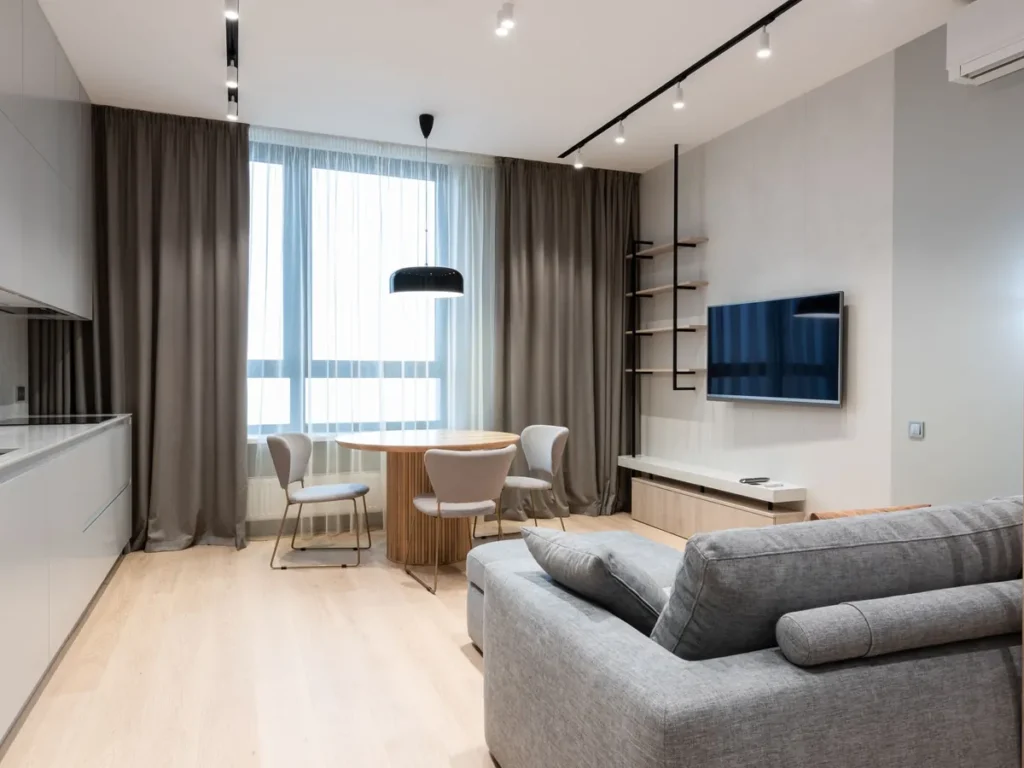 Moderne woonkamer met lichte houten vloer, grijze bank en open keuken